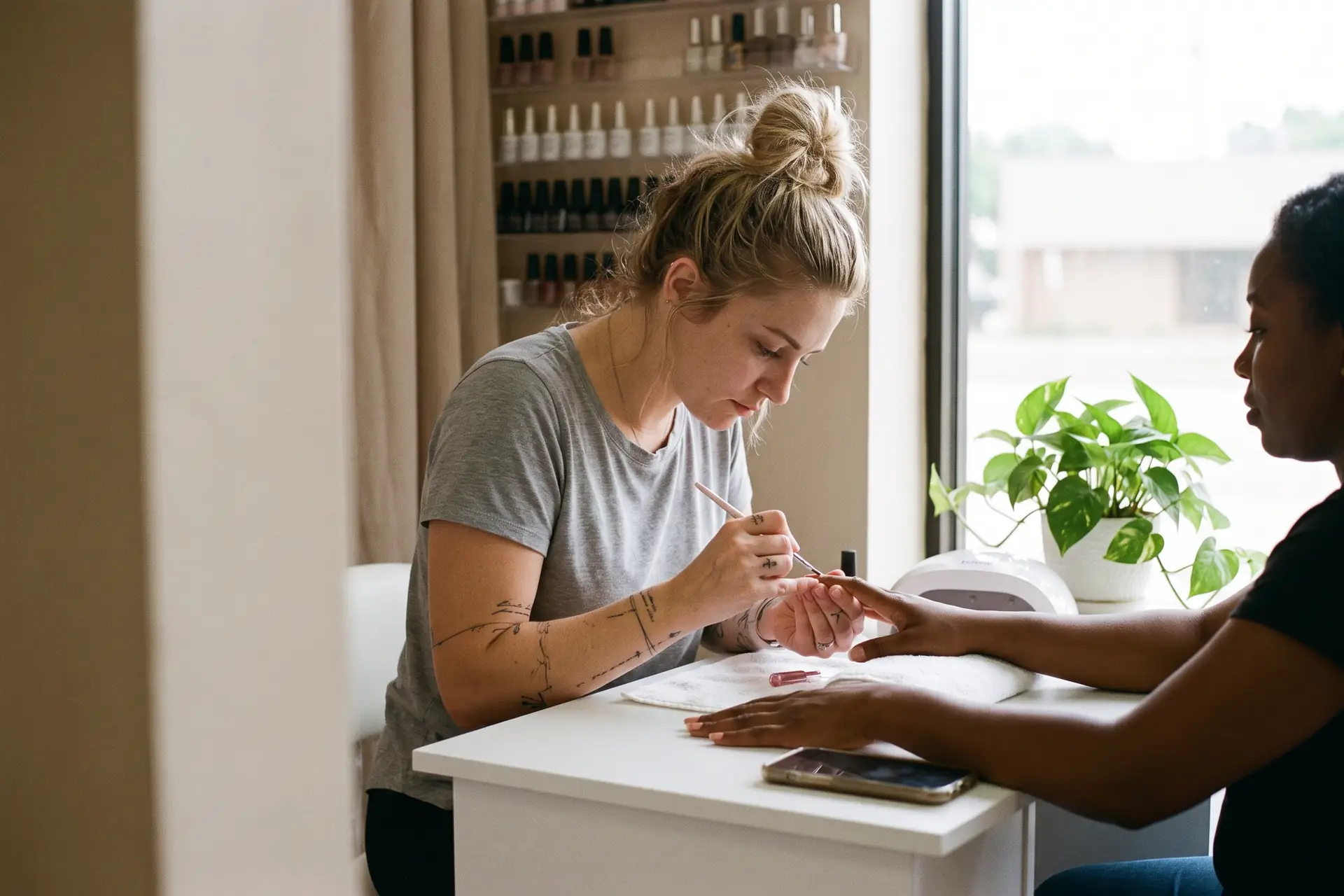 A nail tech paints a client’s gel manicure at a sunny station in an Arlington studio. Sample photo with invented people.