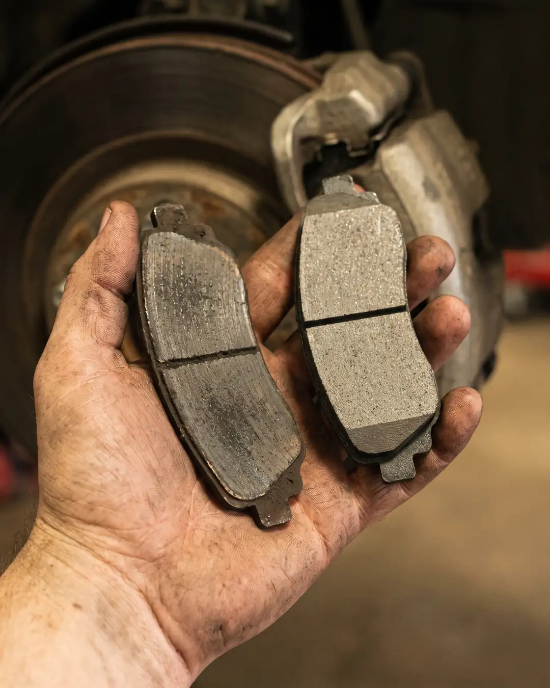 A worn brake pad held next to a new one in a mechanic’s hand. Sample photo.